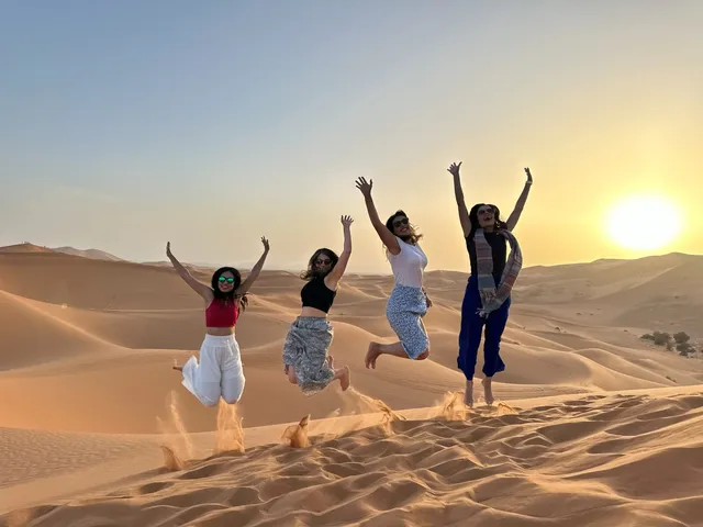 Viajantes pulando nas dunas do Erg Chebbi ao pôr do sol, Merzouga, Marrocos